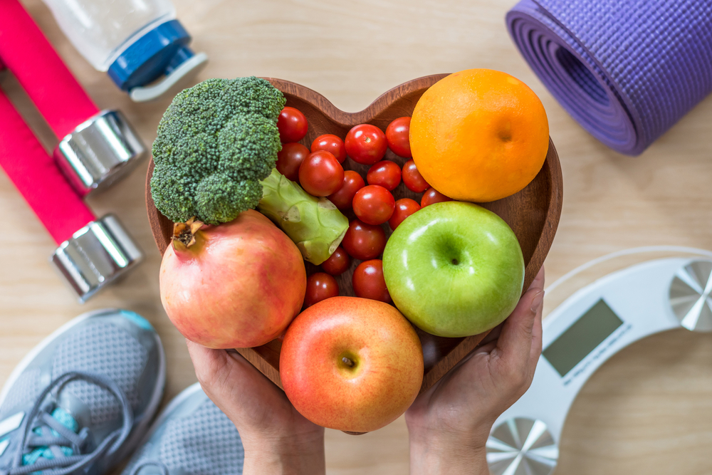 heart-shaped bowl with fruits and vegetables held over exercise equipment