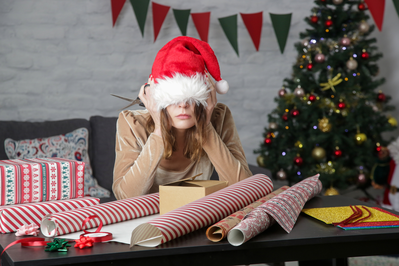 stressed woman pulling santa hat over eyes while wrapping gifts