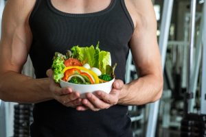 fit man in gym holding bowl of salad