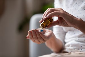 close up of older woman's hands pouring pills into hand from prescription bottle