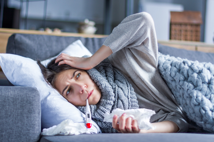 A sick woman on the couch with tissues and a scarf. She needs immune defense vitamins to help fight the flu.