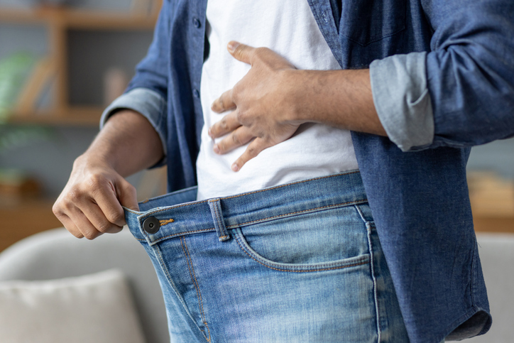 A man shows how much weight he has lost by holding out the waist of his jeans, symbolizing his successful diet aided by berberine supplement benefits