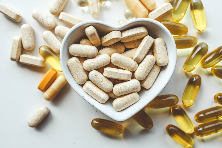 Heart health supplements (tablets and vitamins) on white background, with a heart-shaped bowl in the middle
