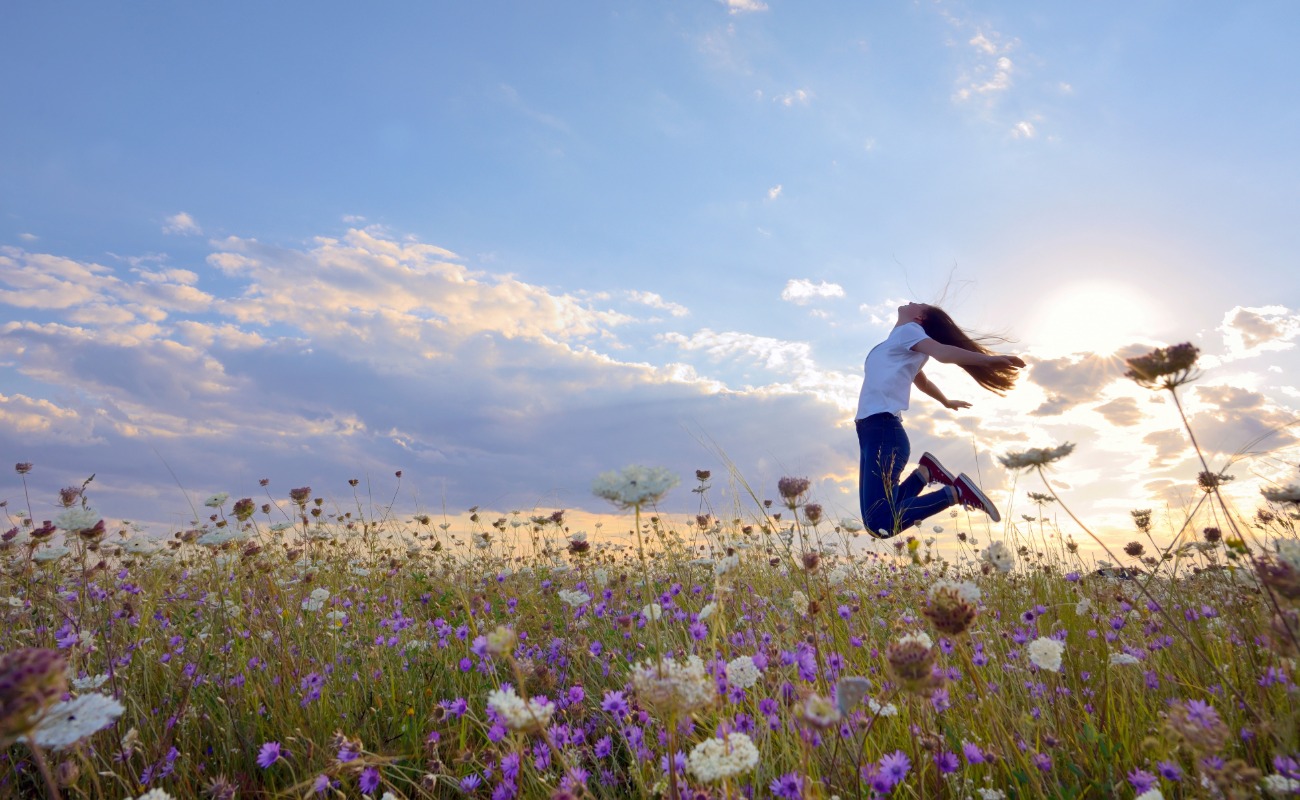 Home Page-1 Happy young woman jumping through a field of flowers on a beautiful spring day.