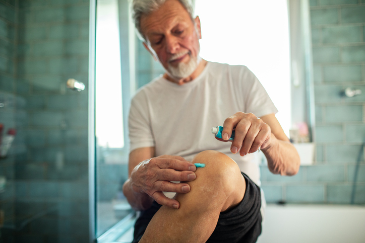 older man applies prescription topical pain relief to his knee