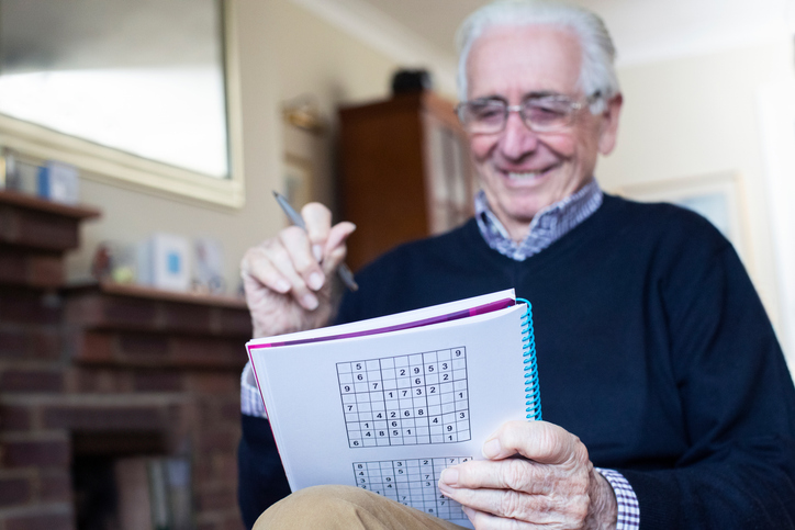 Smiling older man solving a sudoku puzzle in his living room, illustrating an article on magnesium for brain health.